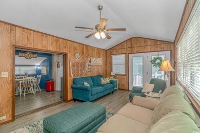 Living room with vaulted ceiling, light hardwood / wood-style flooring, ornamental molding, ceiling fan, and wooden walls