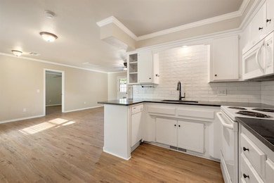 Kitchen featuring ornamental molding, white appliances, tasteful backsplash, white cabinetry, and light wood-style floors