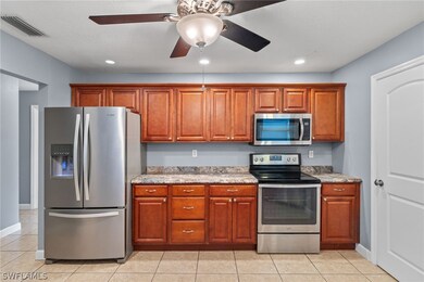 Kitchen with light stone counters, appliances with stainless steel finishes, light tile patterned floors, and ceiling fan