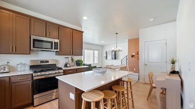 Kitchen featuring appliances with stainless steel finishes, a kitchen bar, light wood-style floors, a chandelier, and a kitchen island