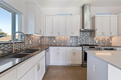 Kitchen featuring dark stone counters, white cabinetry, appliances with stainless steel finishes, wall chimney range hood, and decorative backsplash