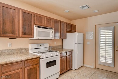 Kitchen featuring white appliances, light stone counters, light tile patterned floors, brown cabinets, and recessed lighting