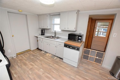 Kitchen with light countertops, white appliances, white cabinets, light wood-type flooring, and ornamental molding