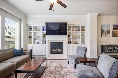 Living room with wood finished floors, crown molding, a glass covered fireplace, ceiling fan, and baseboards