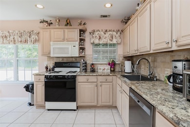 Kitchen featuring range, tasteful backsplash, white microwave, stainless steel dishwasher, and light tile patterned floors