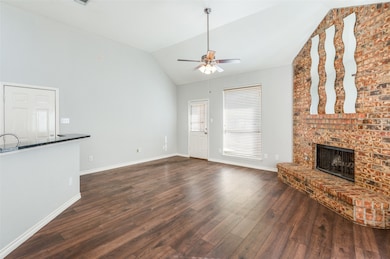Unfurnished living room with lofted ceiling, dark wood-type flooring, a brick fireplace, and a ceiling fan