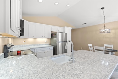 Kitchen with freestanding refrigerator, range with electric stovetop, white cabinetry, decorative light fixtures, and light stone counters