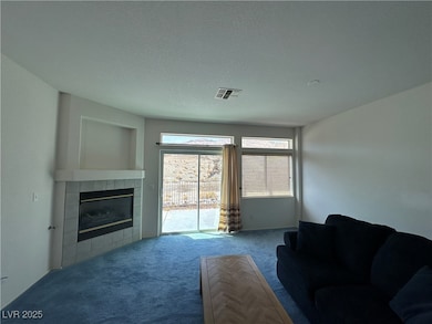 Carpeted living area with a tiled fireplace, visible vents, and a textured ceiling