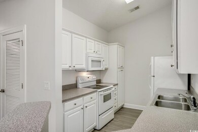 Kitchen with white appliances, white cabinets, light wood-type flooring, light countertops, and a textured ceiling