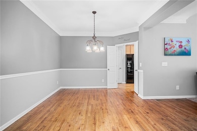 Unfurnished room featuring a chandelier, light wood-style flooring, crown molding, and baseboards