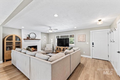 Living room featuring a textured ceiling, light wood-type flooring, a brick fireplace, a ceiling fan, and recessed lighting
