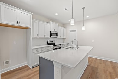 Kitchen with stainless steel appliances, a center island with sink, light wood-style floors, white cabinets, and recessed lighting
