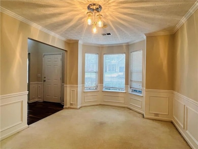 Empty room with a decorative wall, ornamental molding, light carpet, wainscoting, and a textured ceiling