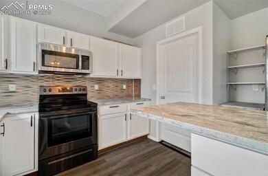 Kitchen featuring appliances with stainless steel finishes, white cabinets, backsplash, dark wood-style flooring, and light stone counters