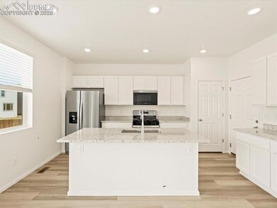 Kitchen with recessed lighting, light stone countertops, white cabinets, stainless steel appliances, and light wood-style flooring