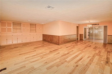 Unfurnished room with a wainscoted wall, light wood-type flooring, a chandelier, and a textured ceiling