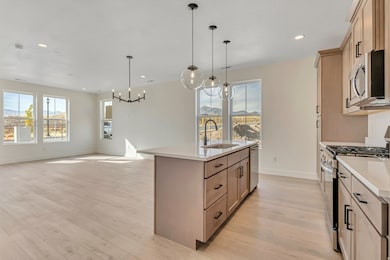 Kitchen featuring stainless steel appliances, open floor plan, hanging light fixtures, a center island with sink, and light wood-style floors