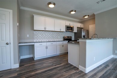 Kitchen with appliances with stainless steel finishes, backsplash, dark stone countertops, dark hardwood / wood-style flooring, and white cabinetry