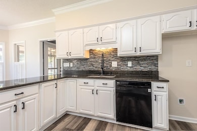 Kitchen featuring black dishwasher, white cabinetry, dark stone countertops, backsplash, and crown molding
