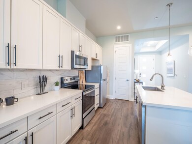 Kitchen featuring stainless steel appliances, decorative light fixtures, dark wood finished floors, backsplash, and white cabinets
