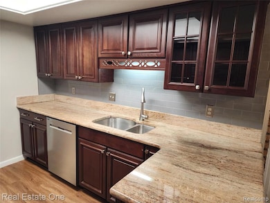 Kitchen with backsplash, light wood-style flooring, dishwasher, dark brown cabinetry, and light stone countertops