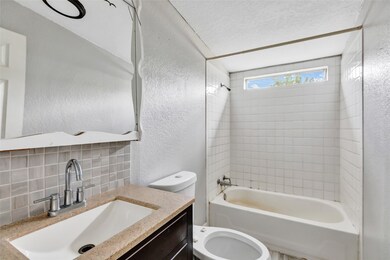 Tiled bathtub shower, single vanity with a modern faucet, and a small window for natural light.