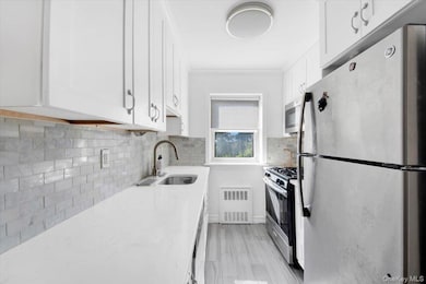 Kitchen with appliances with stainless steel finishes, tasteful backsplash, white cabinetry, and light stone counters