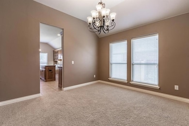 Empty room featuring lofted ceiling, light carpet, a chandelier, healthy amount of natural light, and baseboards