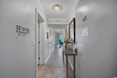 Corridor featuring inlaid floor details, a textured wall, light tile patterned floors, ornamental molding, and a textured ceiling