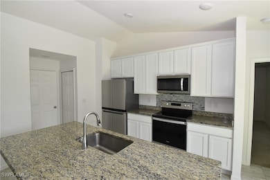 Kitchen featuring appliances with stainless steel finishes, light stone countertops, white cabinets, a kitchen island with sink, and backsplash