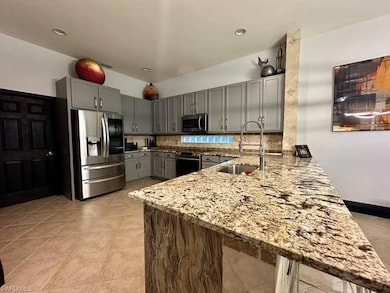 Kitchen with appliances with stainless steel finishes, a peninsula, gray cabinets, light stone countertops, and backsplash
