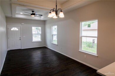 Foyer with a raised ceiling, ceiling fan with notable chandelier, and dark wood-type flooring