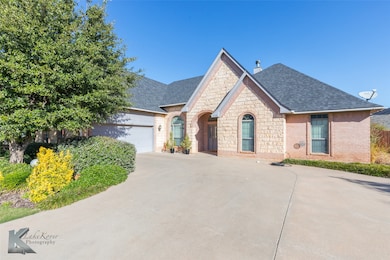 French provincial home with stone siding, roof with shingles, driveway, and brick siding