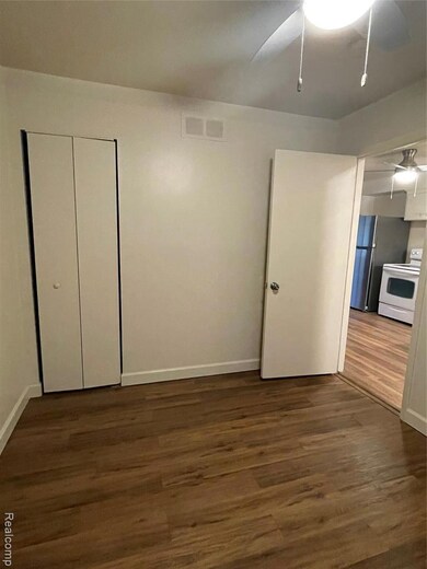 Unfurnished bedroom featuring dark wood-type flooring, a closet, refrigerator, and ceiling fan
