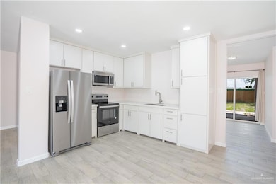 Kitchen with stainless steel appliances, light countertops, white cabinets, light wood-type flooring, and recessed lighting