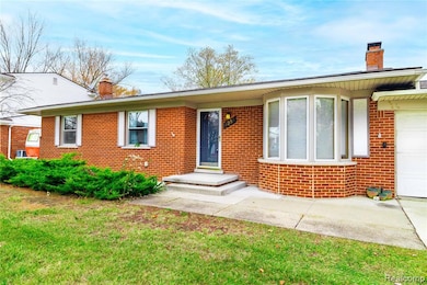 View of front of property featuring a chimney, brick siding, a garage, and a front yard