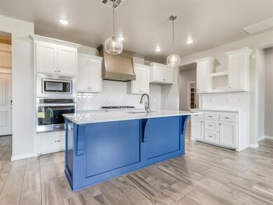 Kitchen featuring appliances with stainless steel finishes, custom range hood, open shelves, decorative backsplash, and white cabinets