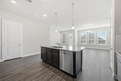 Kitchen with stainless steel dishwasher, wood finish floors, decorative light fixtures, light stone counters, and a center island with sink