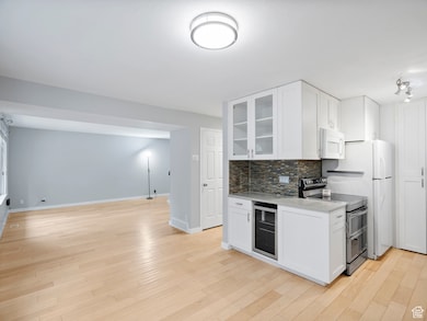 Kitchen with glass insert cabinets, white cabinetry, tasteful backsplash, and white appliances