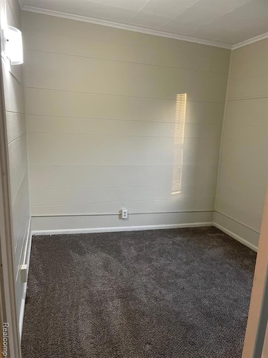 Unfurnished room featuring dark colored carpet and crown molding