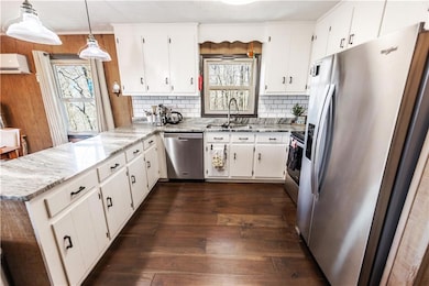 Kitchen with a wall mounted air conditioner, a peninsula, stainless steel appliances, dark wood-type flooring, and a sink