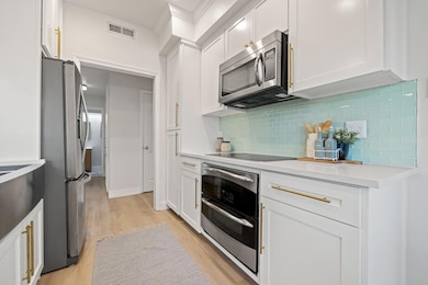 Kitchen featuring white cabinets, light wood finished floors, appliances with stainless steel finishes, tasteful backsplash, and light stone counters