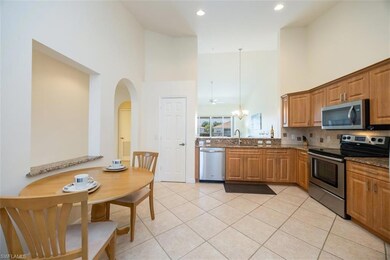 Kitchen with appliances with stainless steel finishes, a high ceiling, dark stone countertops, light tile patterned floors, and hanging light fixtures