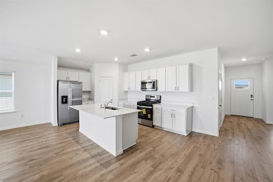 Kitchen with appliances with stainless steel finishes, white cabinetry, a center island with sink, light wood-style floors, and recessed lighting