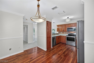 Kitchen with light countertops, stainless steel appliances, dark wood-style flooring, brown cabinetry, and ornamental molding