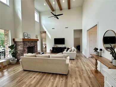 Living area with a fireplace, a high ceiling, light wood-type flooring, ceiling fan, and beam ceiling