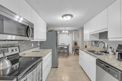 Kitchen featuring stainless steel appliances, tasteful backsplash, light stone countertops, and white cabinetry