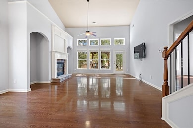 Unfurnished living room featuring a high ceiling, ceiling fan, dark wood-style floors, a glass covered fireplace, and stairway