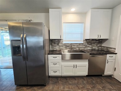 Kitchen with stainless steel appliances, white cabinets, dark stone counters, tasteful backsplash, and plenty of natural light