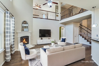 Living room with a lit fireplace, a towering ceiling, dark wood-style flooring, ceiling fan, and arched walkways